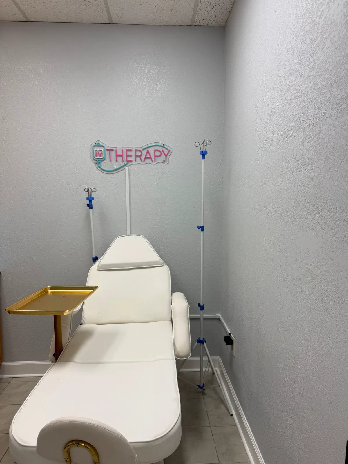 IV therapy room with reclining chair, IV stands, and a neon therapy sign